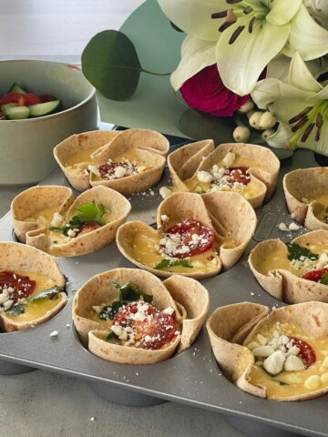 tortilla egg cups in a muffin tray with feta cheese sprinkled on top