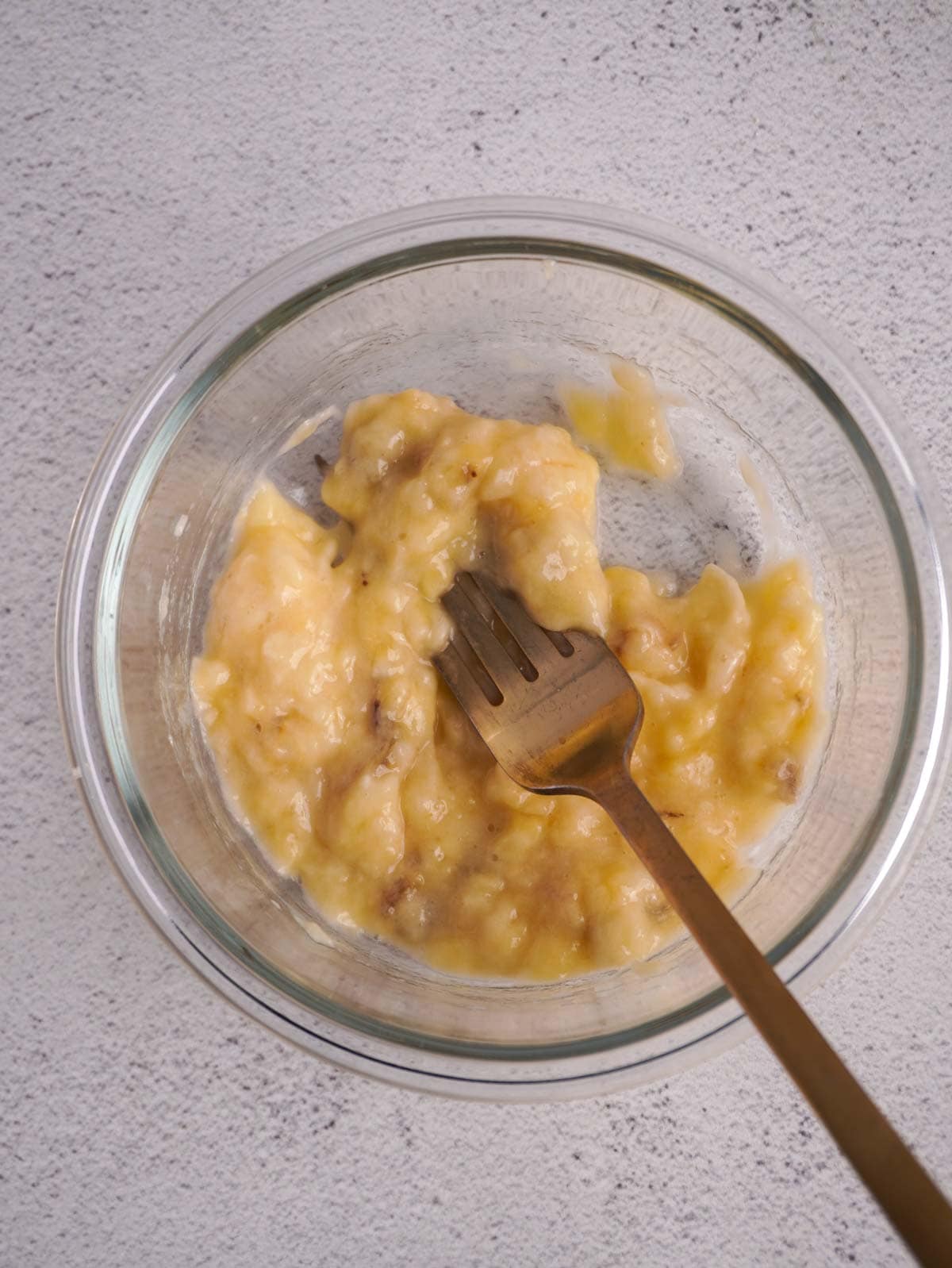 A glass bowl with mashed banana for this protein pancake bowl recipe.