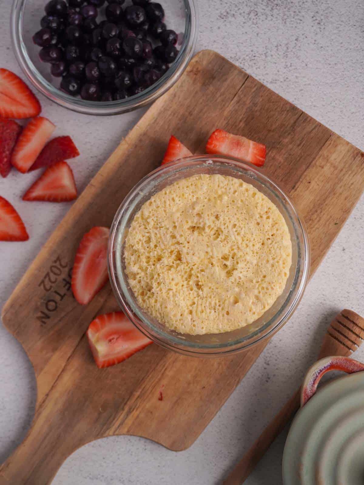 A glass bowl with a cooked vanilla protein pancake inside it and another bowl of berries beside it. 