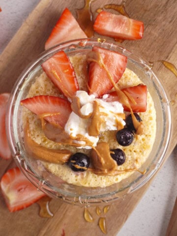 A protein pancake in a microwave safe bowl with berries, greek yogurt and honey drizzled on top.