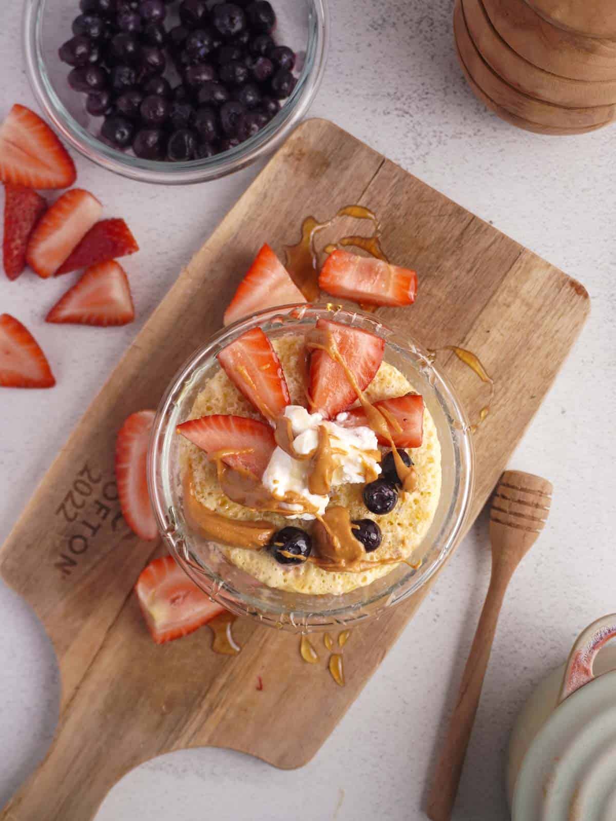 A protein pancake in a microwave safe bowl with berries, greek yogurt and honey drizzled on top. 