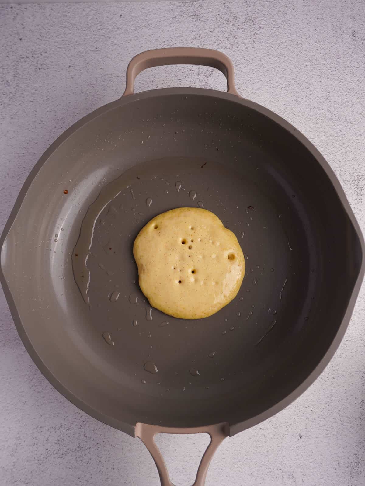 A pancake being cooked on a non stick pan with air bubbles indiciating its ready to be flipped.