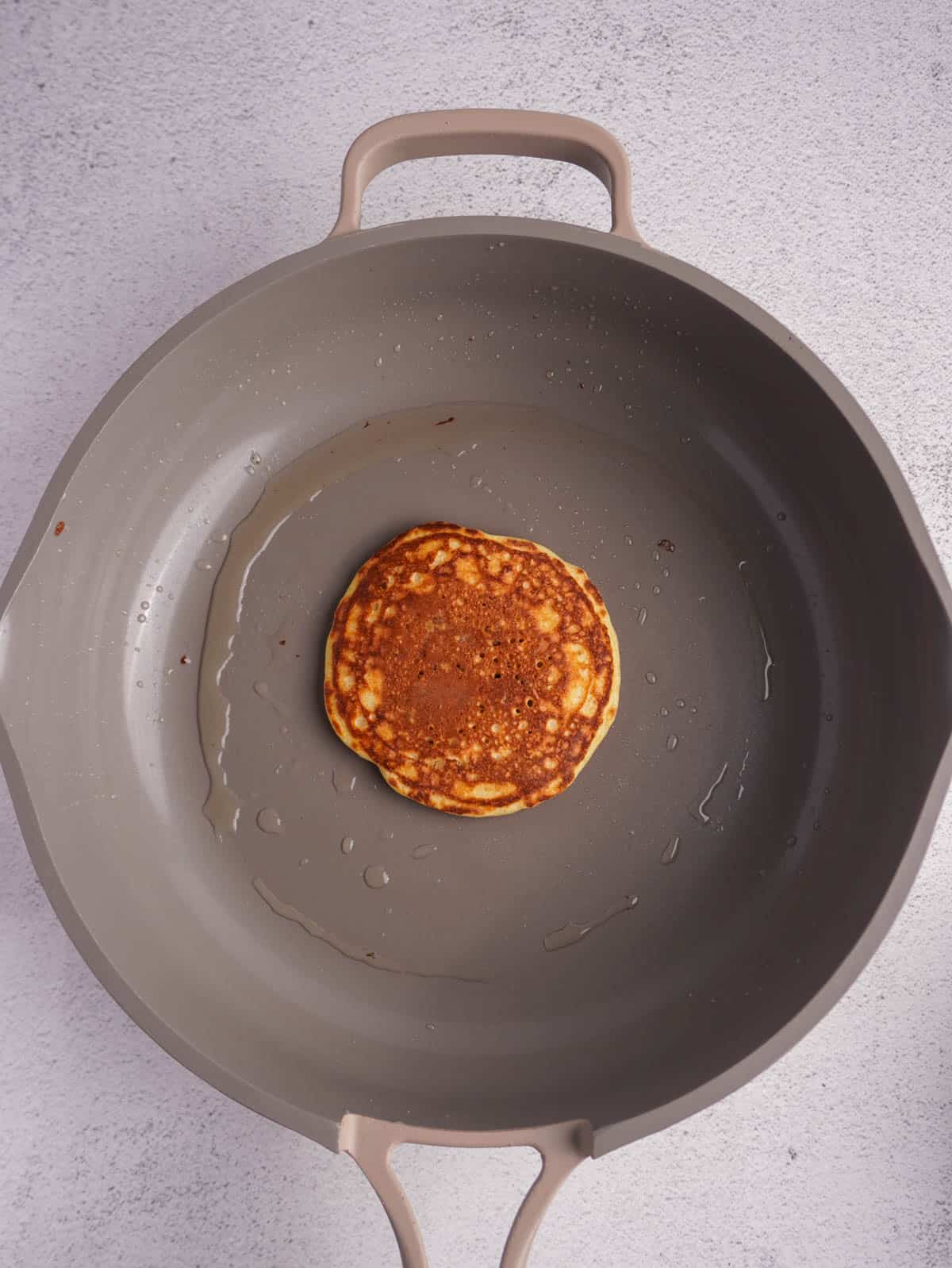 A single golden pancake on a non stick pan.