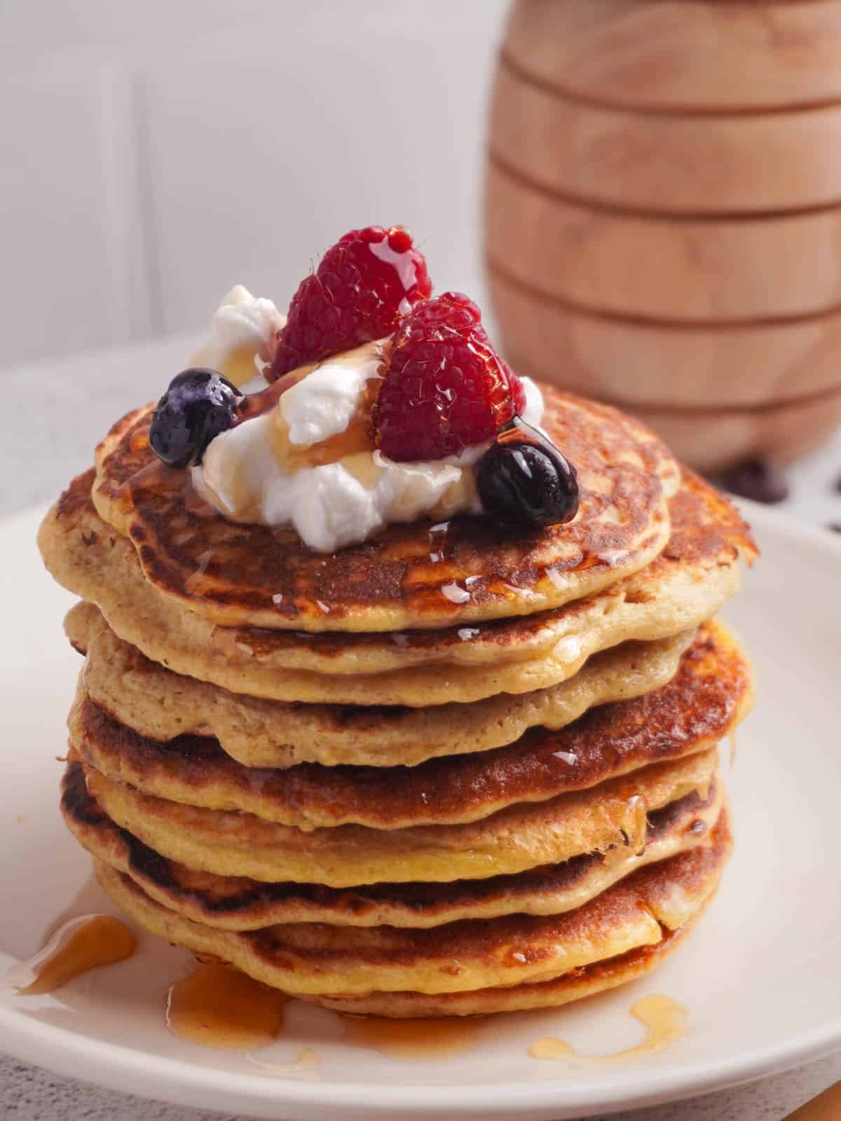 A stack of protein pancakes with greek yogurt, berries and honey drizzled on top.