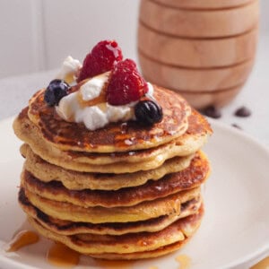 A stack of protein pancakes with greek yogurt, berries and honey drizzled on top.