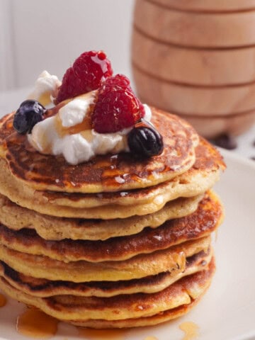 A stack of protein pancakes with greek yogurt, berries and honey drizzled on top.