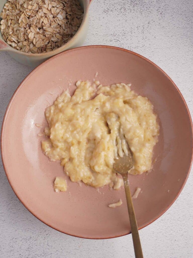 A bowl with a fork in it and a mashed banana.