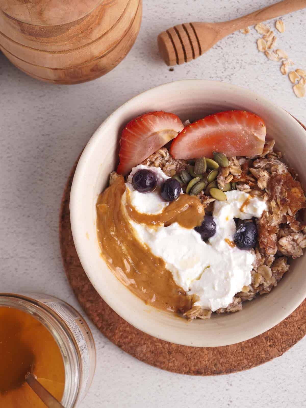 A bowl of scrambled oats with greek yogurt, peanut butter and berries on top. 