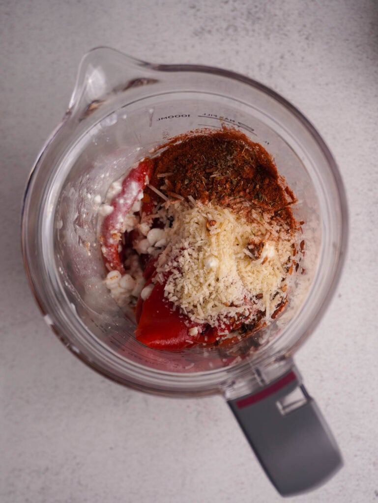 A blender with cottage cheese and roasted peppers inside.