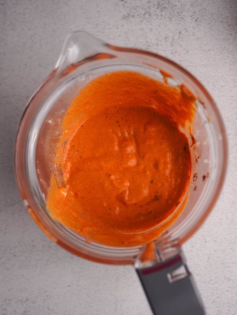 A blender with a creamy red sauce inside it.