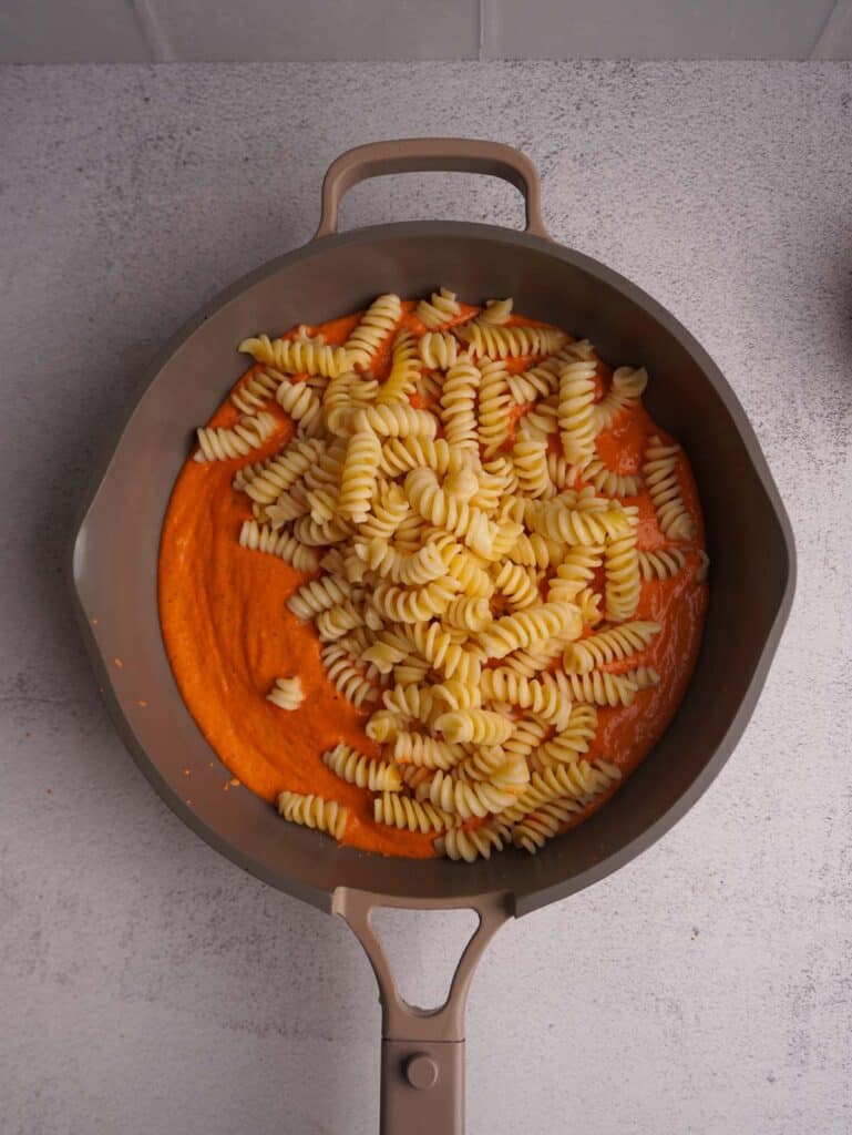 A skillet with a red pasta sauce with some freshly boiled pasta on top.