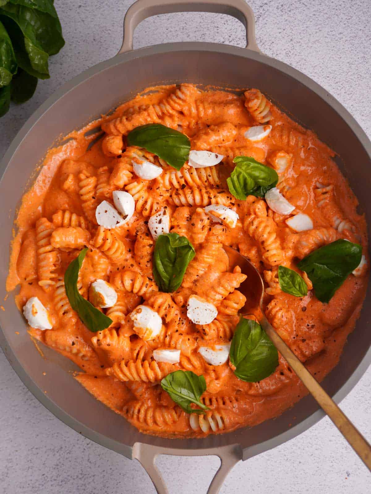 A skillet filled with pasta and a creamy cottage cheese pasta sauce topped with fresh mozzarella and torn basil leaves.