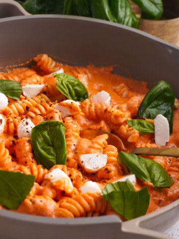 A skillet filled with pasta and a creamy cottage cheese pasta sauce topped with fresh mozzarella and torn basil leaves.