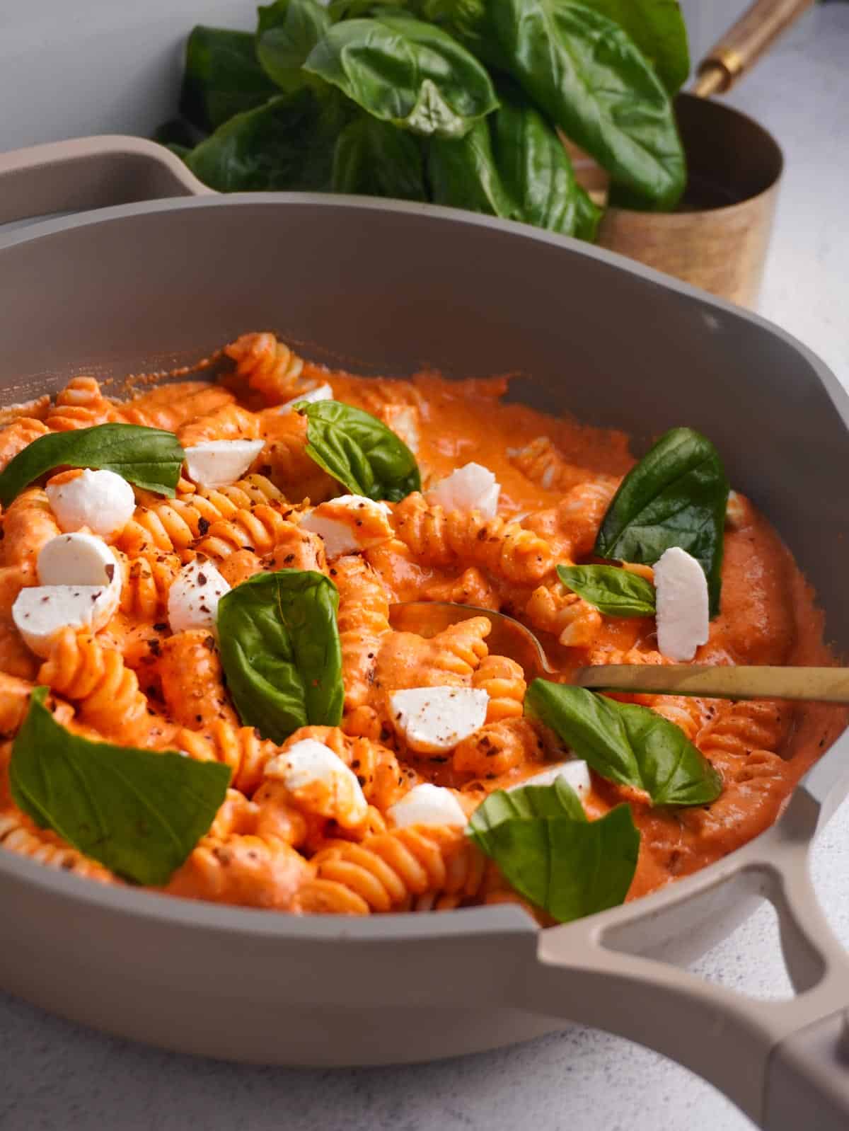 A skillet filled with pasta and a creamy cottage cheese pasta sauce topped with fresh mozzarella and torn basil leaves.